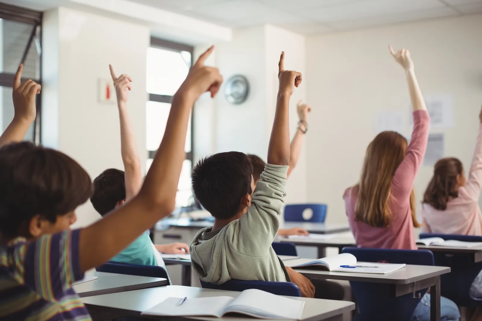 Alumnos levantando la mano en clase con cuadernos abiertos sobre los pupitres