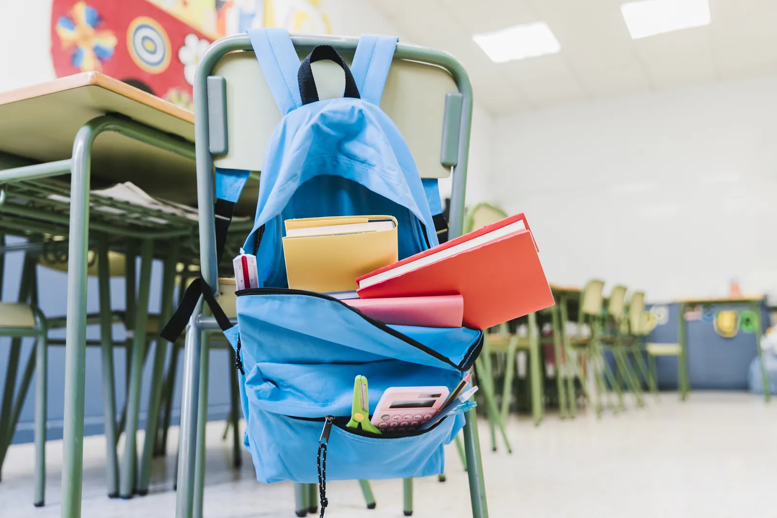 Mochila escolar abierta con libros de texto, carpetas y material escolar en un aula