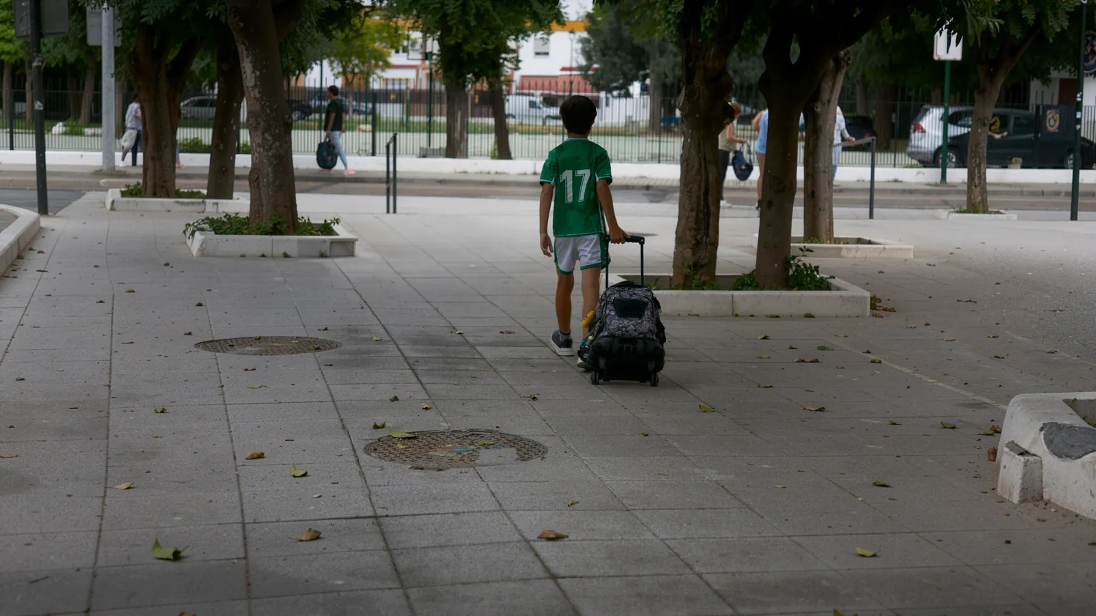 Niño caminando hacia el colegio tirando de una mochila escolar con ruedas